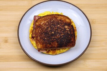 A homemade breakfast sandwich with crispy toasted bread, scrambled eggs, bacon, and melted cheese...