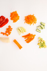 An assortment of freshly cut vegetables and fruits arranged on a white background. Includes carrot,...