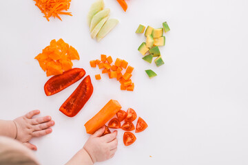 A child's hands reaching for freshly chopped vegetables on a white surface. Includes diced avocado,...