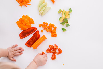 A child's hands reaching for freshly chopped vegetables on a white surface. Includes diced avocado,...