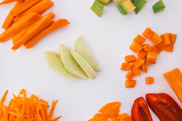 An assortment of freshly cut vegetables and fruits arranged on a white background. Includes carrot,...