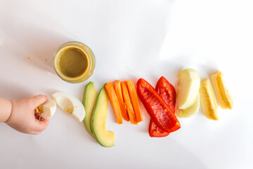 A child's hands reaching for freshly chopped vegetables on a white surface. Includes diced avocado,...