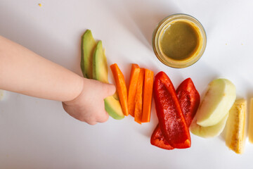 A child's hands reaching for freshly chopped vegetables on a white surface. Includes diced avocado,...