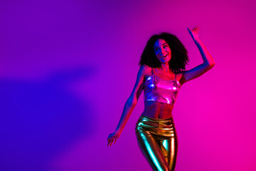 Young stylish woman dancing in vibrant neon lighting, wearing modern shiny outfit, enjoying a fun night at the club
