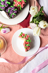 Muffins with candied fruits and cream in the form of tulips on a white plate, homemade pastries for Mother's Day, light composition, muffins with tea, tulips and pink silk ribbons in the background
