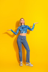 Obraz premium Stylish young woman in casual clothing cheerfully gesturing on a vivid yellow vertical background, expressing happiness