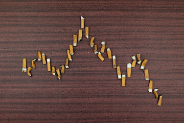 Schedule of smoked cigarettes. Cigarette butts stacked on a wooden background. Drop and damage graph