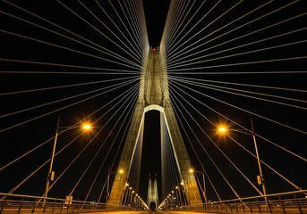 Obraz premium Nighttime CableStayed Bridge Illuminated Structure, Golden Hues, Dark Sky