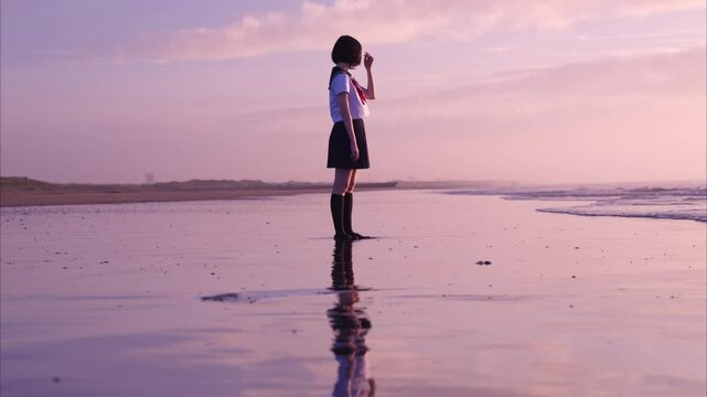 朝焼けの海岸で波打ち際に立つ女子高校生