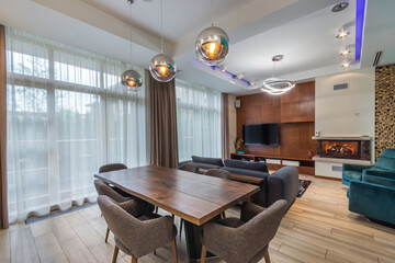 Stylish living room in a private house with panoramic windows. Beautiful lamps, fireplace and upholstered furniture.