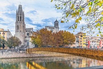 Evening view of Girona featuring the Gothic Sant Feliu Church, the illuminated Pont de Sant Feliu bridge and colorful riverside buildings reflecting in the Onyar River, Spain. Serene autumn atmosphere