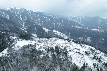 A breathtaking aerial view of Shogran Hill Station covered in snow, surrounded by dense pine...