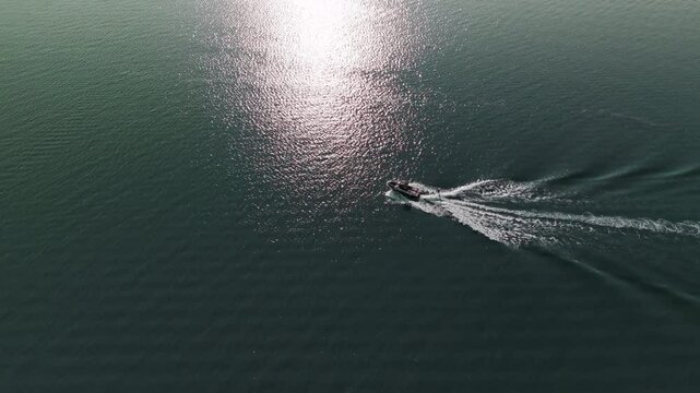 Aerial view of a speedboat moving across a blue water. A person is being towed behind the boat, wakeboarding or water skiing, Carving through the water with a dynamic posture.
