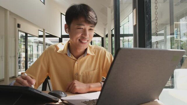Man is sitting at a table with a laptop and a cell phone. He is smiling and he is enjoying himself