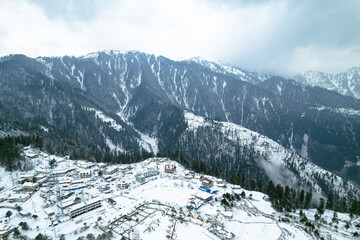 A breathtaking aerial view of Shogran Hill Station covered in snow, surrounded by towering...