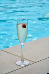 A glass of prosecco in a pool with raspberries in a glass