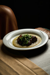 red meat steak with mashed potatoes on a white plate next to a brown leather armchair 