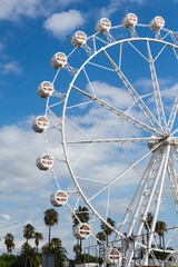 The Ferris wheel in Barcelona, ​​Spain, which is located on a promenade with palm trees against a blue sky with clouds