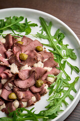 vitello tonnato salad with pork,sauce and olives on a white plate