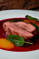 a red meat steak with vegetables and red sauce on a white plate