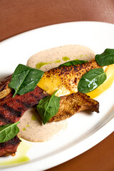 a red meat steak with vegetables and sauce on a white plate