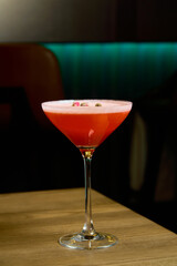 a red cocktail with rose on a brown table on a green background 