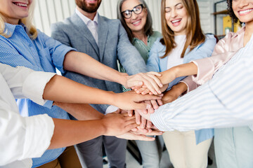 Group of professionals joining hands in a collaborative office setting celebrating teamwork