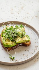 A close-up of freshly made avocado toast topped with microgreens on a ceramic plate.