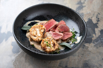 Roasted saddle of venison fillet with bread dumplings in a creamy mushroom sauce served as close-up in a design bowl with a rustic background