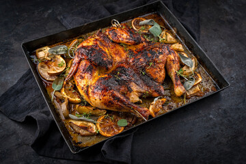 Traditional barbecue spatchcocked chicken al mattone chili with orange and apple slices served as close-up on an old rustic metal tray