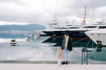 Mom and little girl stand on the embankment next to the moored ships