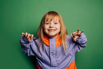 little red-haired girl in a vintage jacket makes funny faces against a green background, playfully expressing herself in a retro-style outfit.