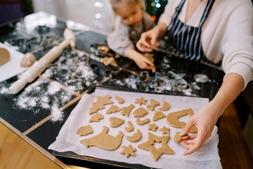Mom places cut out cookies on a baking sheet while sitting at the table with her little daughter....