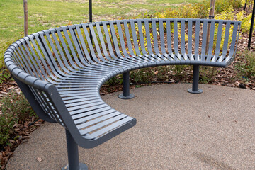 A sleek, curved black metal bench with a contemporary design, placed on a paved pathway in a...