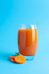 Fresh carrot smoothie in glass and cut vegetable on light blue background