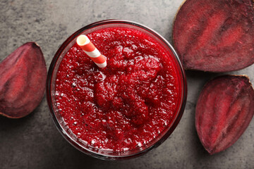 Fresh beetroot smoothie in glass and cut vegetable on grey textured table, flat lay