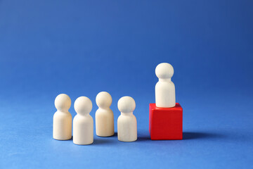 Competition concept. Human figure on wooden cube and other ones behind against blue background