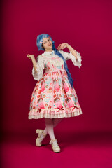 Cosplayer wearing pastel dress and blue wig posing on pink background