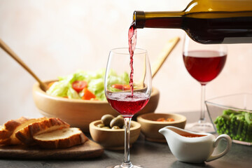 Pouring red wine into glass at grey table with tasty food, closeup