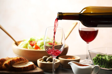 Pouring red wine into glass at grey table with tasty food, closeup
