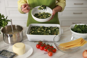 Woman making spinach lasagna at marble table indoors, closeup