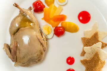 Baked quail is cooked and served with vegetables on a white platter with red sauce.
