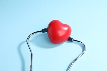 Stethoscope and red decorative heart on light blue background, top view