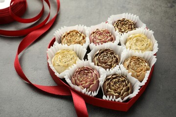 Flower shaped chocolate bonbons in box and red ribbon on grey table, closeup
