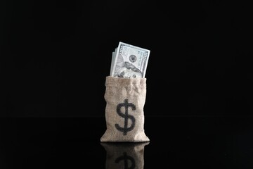 Dollar banknotes in burlap sack on dark mirror surface
