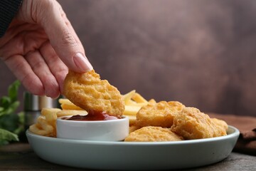 Woman eating tasty chicken nuggets and french fries with sauce at wooden table, closeup. Space for text