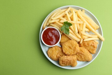 Tasty chicken nuggets and french fries with sauce on green background, top view. Space for text