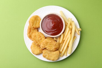 Tasty chicken nuggets and french fries with sauce on green background, top view