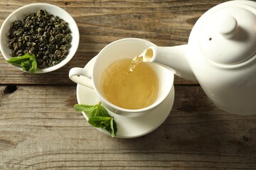 Pouring freshly brewed tea from teapot into cup at wooden table, above view