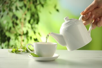 Woman pouring freshly brewed tea from teapot into cup at white marble table outdoors, closeup